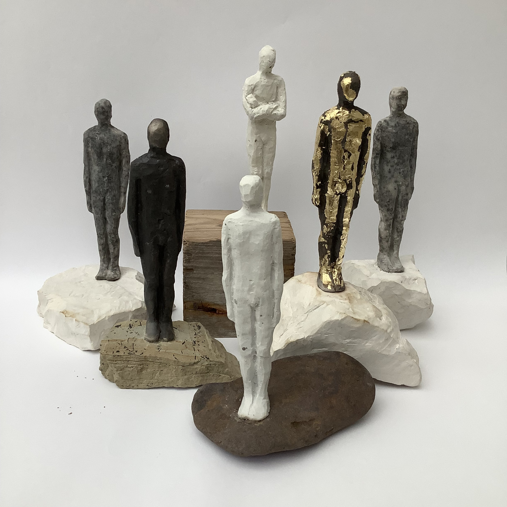 Six sculptures of standing humans in various poses and materials.