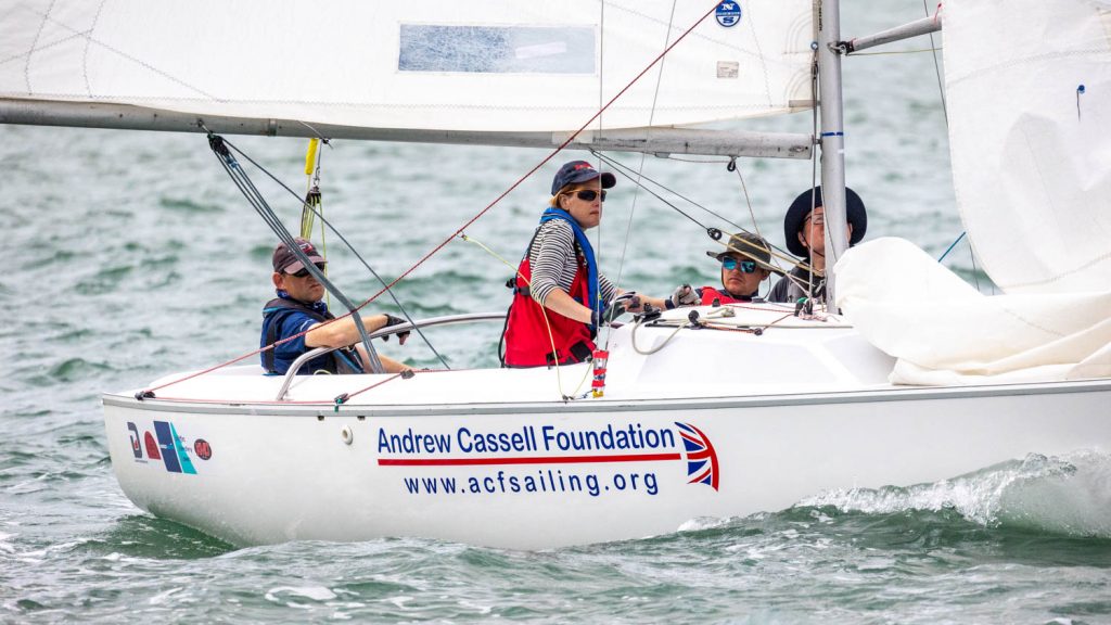 Shows the back half of a sonar keelboat on shiny green water. the boat is going downwind and the four crew are concentrating fiercely