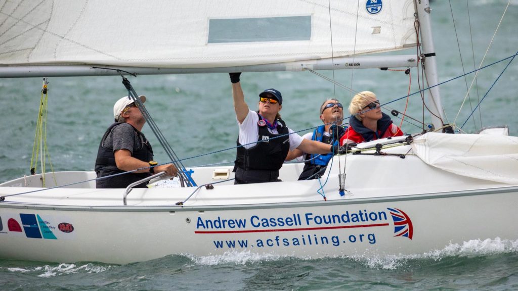 ACF Limbitless racing downwind in moderate wind. The crew are intently focused on keeeping the white keelboat racing well and there is a curl of foam down the side of the boat